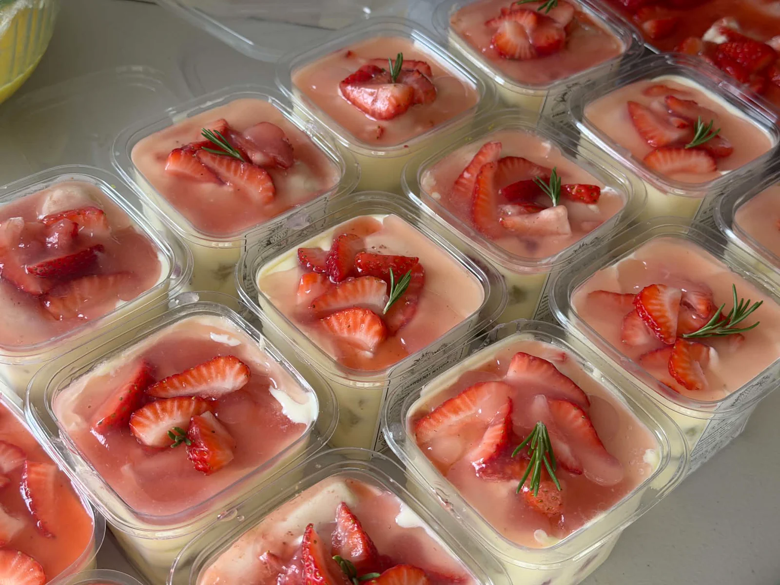 A batch of individual tiramisu cups topped with strawberry sauce and sliced strawberries