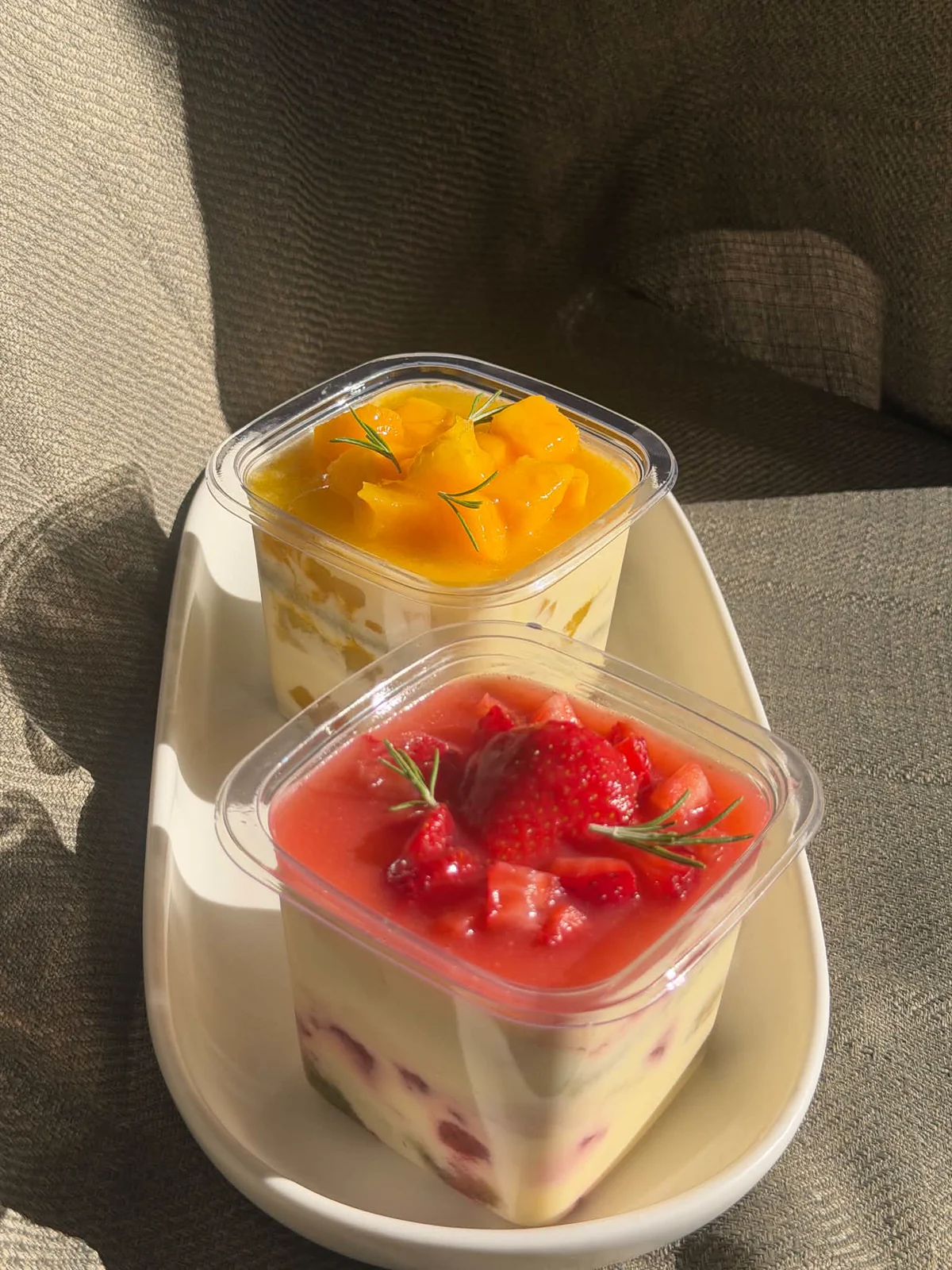 Strawberry and mango tiramisu cups on a white tray in warm sunlight